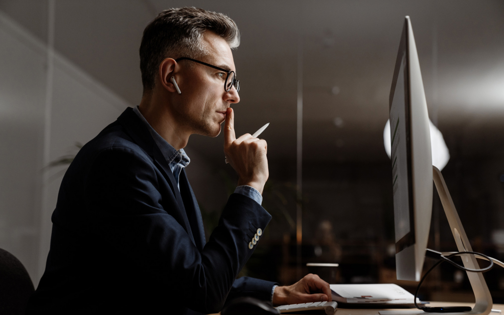 Concentrated Grey Man In Eyeglasses Working With Computer At Office